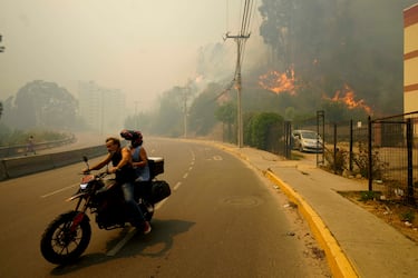 Dos residentes evacuan en una motocicleta mientras el humo causado por los incendios forestales llena el cielo y las llamas se extienden hacia Viña del Mar. 
