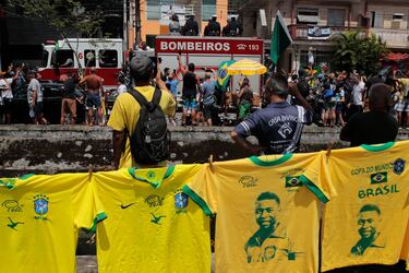 Camisetas que recuerdan a la difunta estrella del fútbol brasileño Pelé cuelgan en una calle mientras un camión de bomberos transporta el ataúd de Pelé al Cementerio Conmemorativo de Santos en Santos.