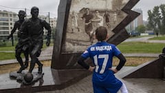 Un joven con un bal&oacute;n observa la estatua que recuerda el Partido del Sitio jugado en San Petersburgo en 1942.