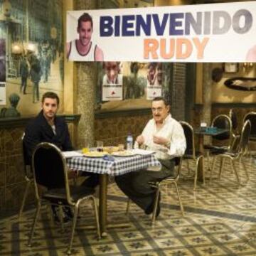 Rudy, sentado con Mariano delante de un cartel de bienvenida.