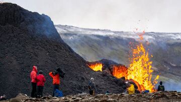 People get up close as lava flows from the erupting Fagradalsfjall volcano some 40 km west of the Icelandic capital Reykjavik, on March 23, 2021. - Hikers took the opportunity to inspect the area where a volcano erupted in Iceland on March 19, some 40 kil