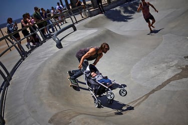 Un skater se desliza sobre un patín mientras empuja un carrito de bebé con una muñeca en el Venice Skatepark de Los Ángeles, uno de los lugares más emblemáticos del sur de California. Ubicado frente al Océano Pacífico, en el paseo marítimo de Venice Beach, este parque es un punto obligado de reunión para turistas, fotógrafos y amantes del skate.