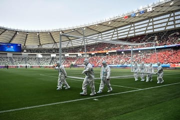 Varios trabajadores, con equipos de protección personal (EPP), transportan una portería del estadio del Centro Deportivo Olímpico de Suzhou, en la provincia de Jiangsu (China), durante los momentos previos al partido de fútbol femenino de los playoffs de clasificación para los Juegos de Tokio 2020 entre China y Corea del Sur.