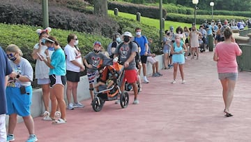 Guests wearing protective masks wait to pick up their tickets at the Magic Kingdom theme park at Walt Disney World on the first day of reopening, in Orlando, Florida, on July 11, 2020. - In the distance at right is the newly repainted Cinderella Castle. D