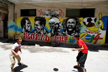 Niños palestinos juegan con un balón frente a un grafiti en el campo de refugiados de Khan Yunis, en el sur de la Franja de Gaza, que representa a futbolistas que participaron en el Mundial de Brasil 2014. De izquierda a derecha: Cristiano Ronaldo de Portugal, Lionel Messi de Argentina, Arjen Robben de Holanda y Andrea Pirlo de Italia.