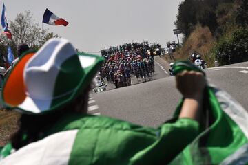 A fan wearing a hat waves a flag as the pack arrives in background during the sixteenth stage of the 106th edition of the Tour de France cycling race between Nimes and Nimes, in Nimes, on July 23, 2019. (Photo by JEFF PACHOUD / AFP)