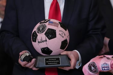 El presidente Donald Trump recibe una camiseta personalizada del Inter Miami, un reloj y un balón de fútbol con un brillante trofeo durante un evento en honor al Inter Miami, campeón de la Major League Soccer de 2025, en la Sala Este de la Casa Blanca.
