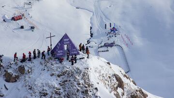 Vista aérea de la cima de la cara por la que los atletas del Freeride World Tour (FWT) 2021 descendieron, con los esquiadores esperando en la puerta de salida junto a la cruz y la línea de meta al fondo, repleta de nieve.