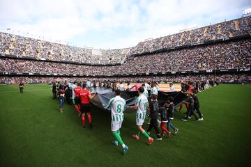 Jugadores del Real Betis y del Valencia CF portan una bandera en homenaje a las vctimas de la DANA.