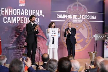 El capitán del Real Madrid de baloncesto, Sergio Llull, y el presidente del club, Florentino Pérez, aplauden a la presidenta de la Comunidad de Madrid, Isabel Díaz Ayuso, que sostiene una camiseta del equipo con su nombre serigrafiado.
