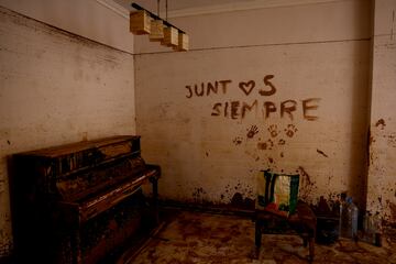 Un texto que dice "siempre juntos" se exhibe en una pared cerca de un piano cubierto de barro, dentro de una residencia que está siendo limpiada por voluntarios, luego de las inundaciones provocadas por las fuertes lluvias, en Massanassa.