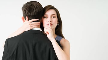 I have a secret. Portrait of a young girlfriend making eye contact and putting a finger on her mouth while hugging her boyfriend or husband