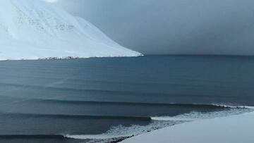 Tres olas perfectas de derechas rompen en el Ártico con una montaña completamente nevada de fondo.