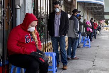 Francisco Montero (center) of Richmond wears a mask while waiting with other in a long line outside of Terra Nova Clinic in the Fruitvale neighborhood of Oakland, Calif.