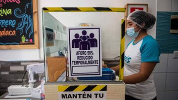 An employee stands next to a sign reading &quot;Temporarily reduced capacity 50%&quot; at a restaurant in Lima on July 20, 2020, mid the new coronavirus pandemic. - The restaurants of Peru, a country with world famous gastronomy, reopened their doors Monday after four months of confinement due to the new coronavirus pandemic, but hundreds did not manage to survive the quarantine. (Photo by ERNESTO BENAVIDES / AFP)