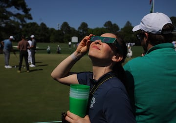 Una aficionada, con gafas protectoras para ver el eclipse solar, observan el eclipse solar durante el Masters de Augusta.