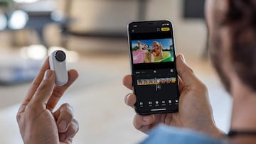 Una persona sujeta con una mano la diminuta cámara de acción Insta360 Go 2 mientras con la otra sujeta el teléfono, con la app abierta.