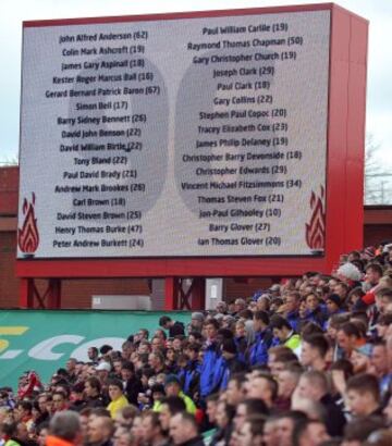 Espectadores durante el minuto de silencio por el 25 ° aniversario del desastre de Hillsborough, con una cartelera en el fondo que muestra los nombres de los que fueron asesinados, por delante del partido de fútbol Inglés Premier League entre el Stoke City y el Newcastle United en el Estadio Britannia en Stoke on Trento 