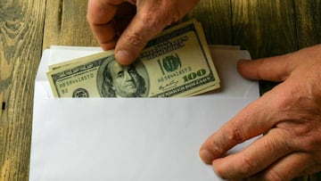 Persona metiendo dinero a un sobre vía Getty Images.