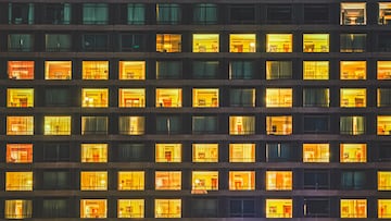 Building facade shows a windows and rooms pattern at night. The exterior features illuminated and dark living spaces with people living like neighbours in a shared communal space. Copenhagen, Denmark