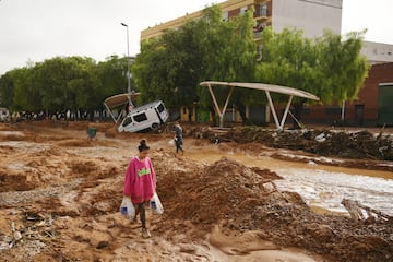 Una mujer camina por calles cubiertas de barro entre coches amontonados después de que una inundación repentina azotara la región el 30 de octubre de 2024 en Valencia, España