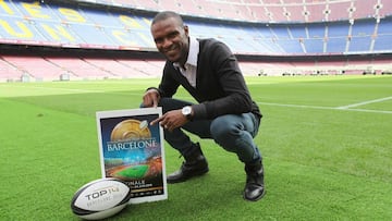 Eric Abidal posa sobre el c&eacute;sped del Camp Nou junto con el cartel de la final de la final del Top 14 de rugby y un oval.