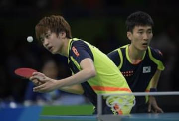 South Korea's Jeoung Young-Sik serves next to South Korea's Lee Sangsu (R) in the men's team qualification round table tennis match against Brazil's Hugo Calderano and Brazil's Gustavo Tsuboi at the Riocentro venue during the Rio 2016 Olympic Games in Rio