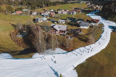 Esta imagen aérea de la localidad austriaca de Riezlern muestra a un grupo de aficionados al esquí de fondo practicando su deporte favorito por una pista que discurre entre prados muy cerca de las viviendas. Las cálidas temperaturas de los últimos días han hecho que se vean notablemente reducidas las habituales zonas esquiables.