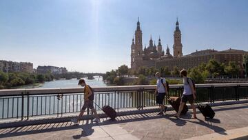 ZARAGOZA 15/08/2020.-El 15 de agosto es quizás uno de los días más importantes del verano en España. Más de un millar de localidades homenajean a sus patrones locales este día , fiestas que este año pasarán desapercibidas por la pandemia del coronavirus. En la imagen, varias personas con maletas cruzan el Puente de Santiago, de Zaragoza.EFE/JAVIER BELVER