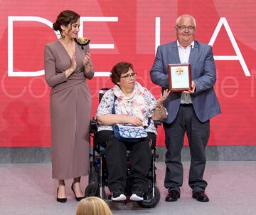 La presidenta de la Comunidad de Madrid, Isabel Díaz Ayuso (i), entrega uno de los galardones al obrero de la construcción Jacinto Tapusa (d), que lo recoge acompañado de su esposa Remedios Pérez.