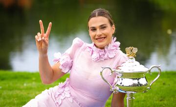 Aryna Sabalenka posando, haciendo el gesto de victoria con los dedos índice y corazón, con el trofeo de campeona del Abierto de Australia en los Jardines Reales de Melbourne.