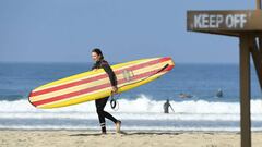 Newport Beach, California, Estados Unidos: Una surfista pasea con su tabla de surf por la playa a pesar del cierre de playas que se decret&oacute; en la zona para intentar frenar el avance de la pandemia de coronavirus. (Wally Skalij/Los Angeles Times/Con