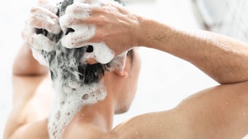 Closeup young man washing hair with with shampoo in the bathroom, health care concept, selective focus
