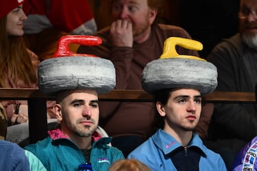 Los seguidores de cualquier deporte apoyan de manera incondicional y muestran su pasión incluso en su indumentaria. El curling no es ajeno a ello, como muestra esta fotografía, en la que se observa a dos aficionados que portan piedras como gorros durante el partido por la medalla de bronce femenino que enfrentó a Canadá y Estados Unidos.