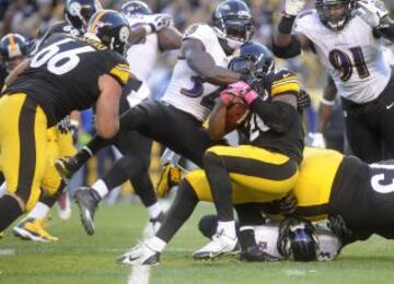 Le'Veon Bell de los Pittsburgh Steelers protege el balón de James Ihedigbo de los Baltimore Ravnes.