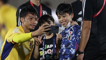 Japan's Gaku Shibasaki uses a mobile phone to take a selfie with schoolchildren at a training session in Al Sadd SC in Doha on November 14, 2022, ahead of the Qatar 2022 World Cup football tournament. (Photo by ADRIAN DENNIS / AFP)