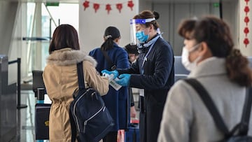 An airline worker wearing a face mask as a preventive measure against the Covid-19 coronavirus gives a passenger alcohol gel to wash her hands at Tianhe International Airport in Wuhan, China's central Hubei province on February 12, 2021. (Photo by Hector RETAMAL / AFP)
