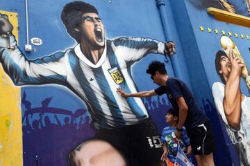 A man and his child pay tribute next to a mural depicting Argentine football legend Diego Maradona at La Boca neighborhood, in Buenos Aires
