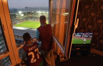 Estos seguidores del West Ham observan el partido de su equipo desde la ventana de su casa. Además lo tienen en la tele para poder ver las repeticiones. Lo único que se echa en falta en la imagen es el cátering.