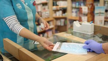 Una farmacéutica vende una mascarilla a un ciudadano.