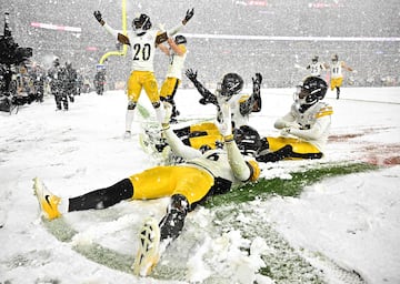 Donte Jackson de los Pittsburgh Steelers celebra con sus compañeros una intercepción haciendo ángeles sobre la nieve.