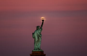 La Luna de las Flores se eleva entre las nubes detr¨¢s de la Estatua de la Libertad al atardecer en la ciudad de Nueva York.