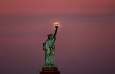 La Luna de las Flores se eleva entre las nubes detrás de la Estatua de la Libertad al atardecer en la ciudad de Nueva York.