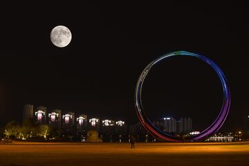 La luna llena del cazador se eleva en el cielo nocturno sobre una noria el 16 de octubre de 2024 en Weihai, provincia de Shandong, China.