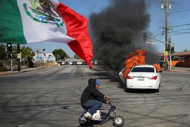 Una bandera mexicana ondea frente a un coche quemado en Compton, California. La imagen es una de las más comunes de las protestas del fin de semana en Los Ángeles. 