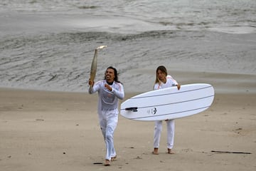 El surfista francés Edouard Delpero (izquierda) corre con la llama olímpica flanqueado por la surfista Zoe Grospiron (derecha).