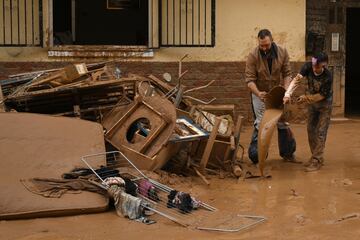 Vecinos intentan limpiar el barro y las pertenencias de sus hogares después de la reciente inundación repentina en el cercano municipio de Alfafar