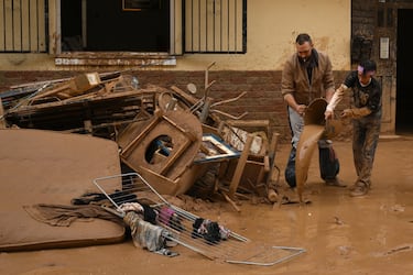 Vecinos intentan limpiar el barro y las pertenencias de sus hogares después de la reciente inundación repentina en el cercano municipio de Alfafar