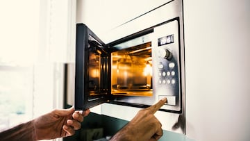 A man using a microwave oven. His finger on the opening button.