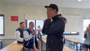 Los alumnos de Rossmoyne Senior High School (Perth, Australia), uniformados, presencian c&oacute;mo el profesor de educaci&oacute;n outdoor se emociona y se pone las manos en la cara al regalarle una tabla de surf. 